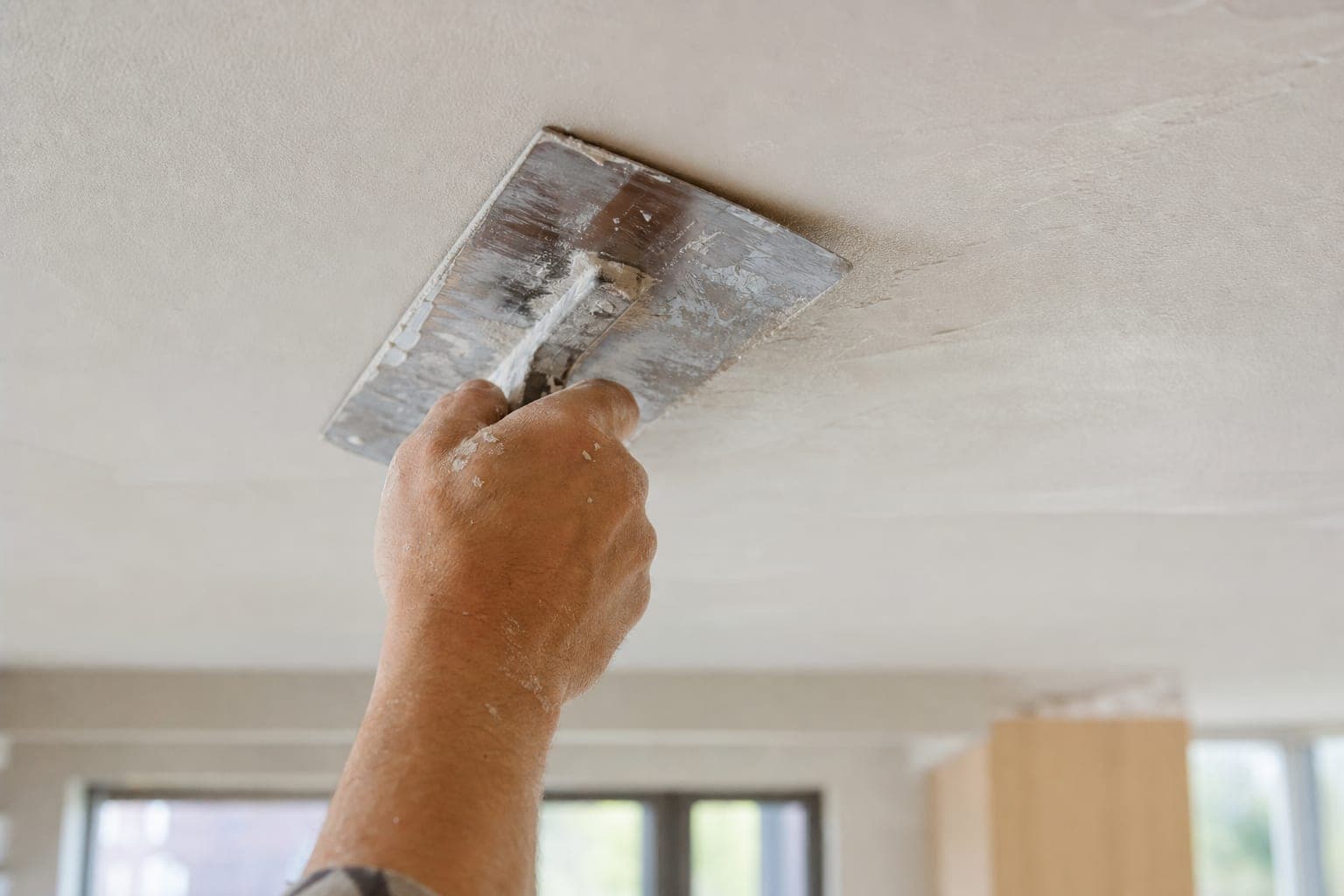Close-up van een hand die met een spaan een plafond gladstrijkt